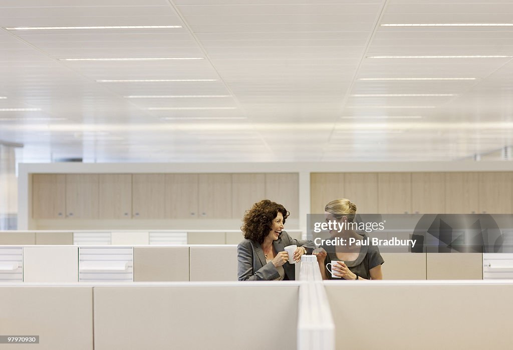 Businesswomen com café gossiping no escritório cubicles