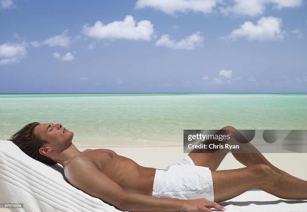 Man on beach sunbathing on lounge chair with eyes closed