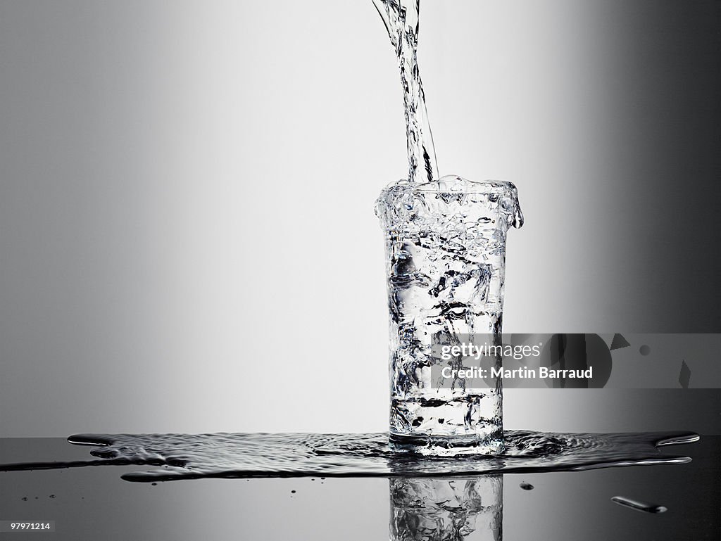 Water pouring into glass and overflowing