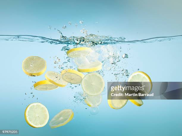 sliced lemons splashing in water - lemon stock pictures, royalty-free photos & images