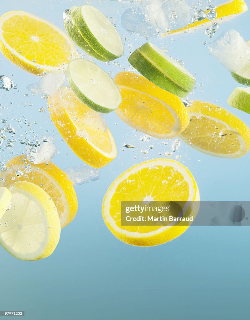 Close up of sliced lemons and limes splashing in water