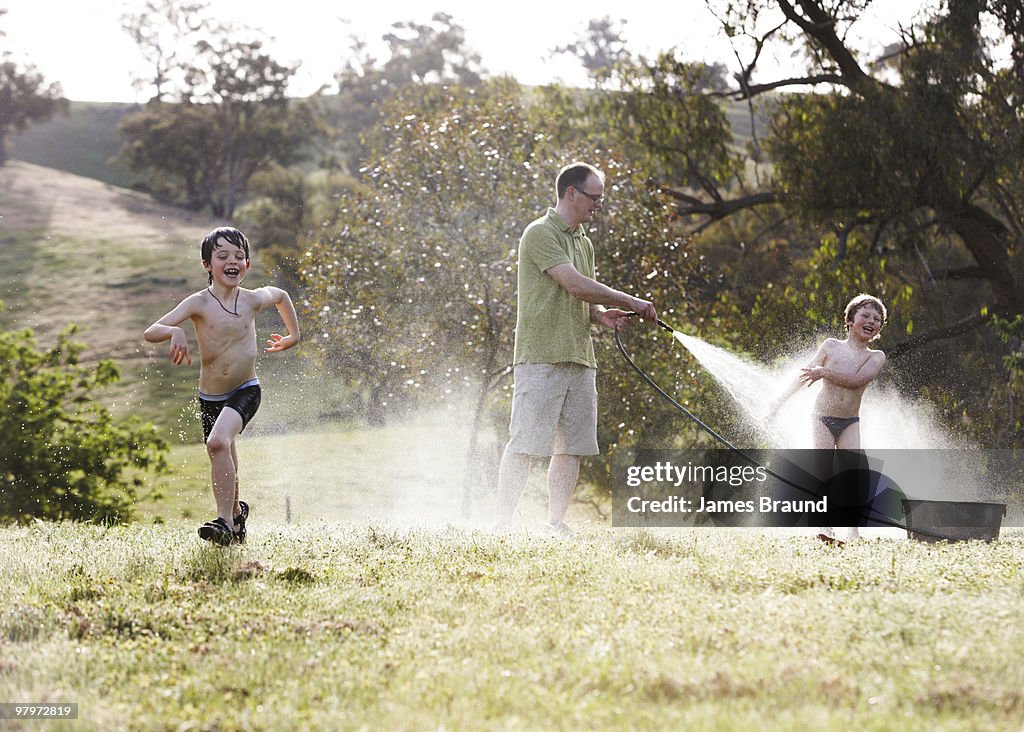 Father spraying children with hose