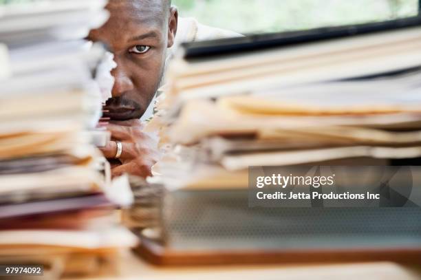 african businessman hiding behind stack of paperwork - overwerkt stockfoto's en -beelden