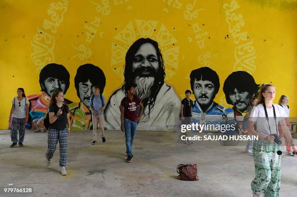 This picture taken on June 18 tourists gather in front of a mural of The Beatles and Maharishi Mahesh Yogi at the now-derelict ashram attended by The...