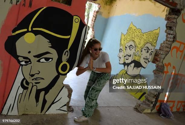 This picture taken on June 18 a tourist poses for a picture next to a mural at the now-derelict ashram attended by The Beatles 50 years ago in...