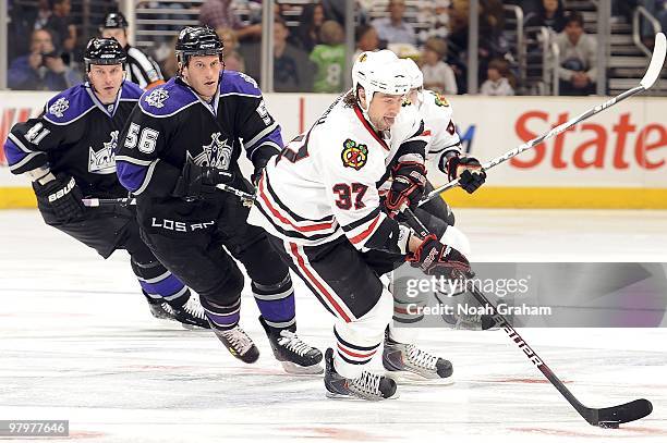 Raitis Ivanans and Richard Clune of the Los Angeles Kings race for the puck against Adam Burish the Chicago Blackhawks during the game on March 18,...