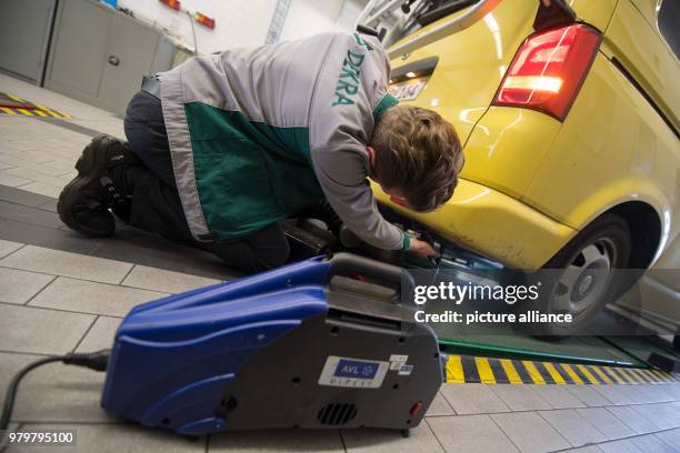 March 2018, Germany, Stuttgart: An employee of the vehicle inspection company Dekra fixes a probe onto the exhaus pipe of a VW T5 diesel with...