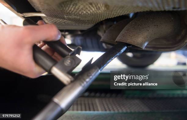 March 2018, Germany, Stuttgart: An employee of the vehicle inspection company Dekra fixes a probe onto the exhaus pipe of a VW T5 diesel with...