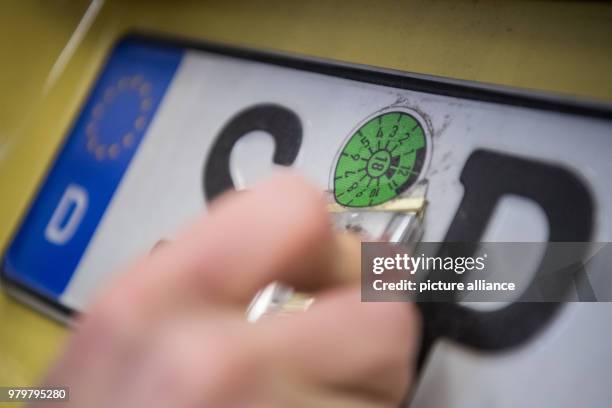 March 2018, Germany, Stuttgart: An employee of the vehicle inspection company Dekra removes a main inspection sticker on the license plate of a VW T5...