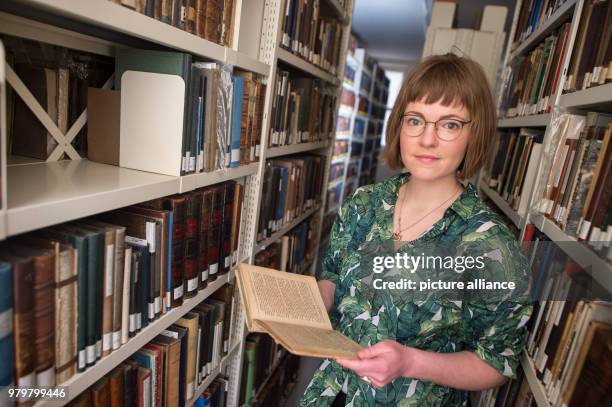 March 2018, Germany, Magdeburg: Historian Elena Kiesel holds an old edition of the book series 'Nesthaekchen' in her hand she stands between shelves...