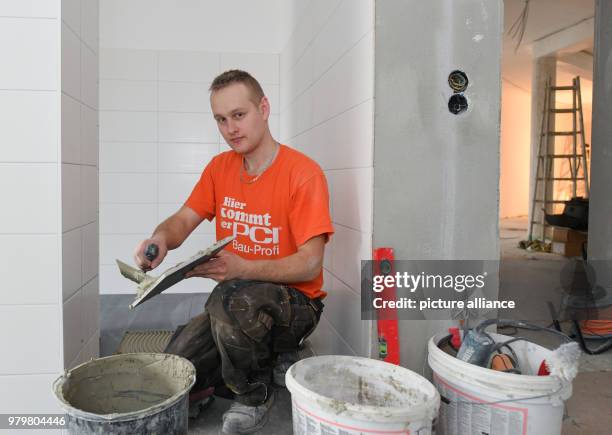 March 2018, Germany, Wiesenau: The Polish tiler trainee Robert Korte installs tile flooring in a bathroom. Robert Korte learned his craft at a German...