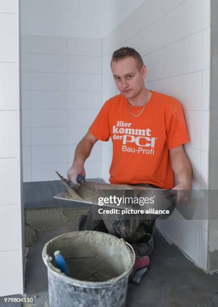 March 2018, Germany, Wiesenau: The Polish tiler trainee Robert Korte installs tile flooring in a bathroom. Robert Korte learned his craft at a German...