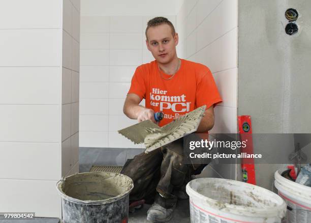 March 2018, Germany, Wiesenau: The Polish tiler trainee Robert Korte installs tile flooring in a bathroom. Robert Korte learned his craft at a German...