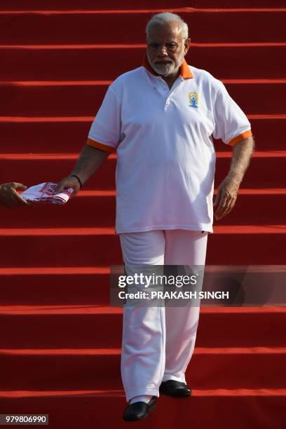 Indian Prime Minister Narendra Modi is handed a scarf as he walks down steps to participate in a mass yoga session along with other practitioners to...