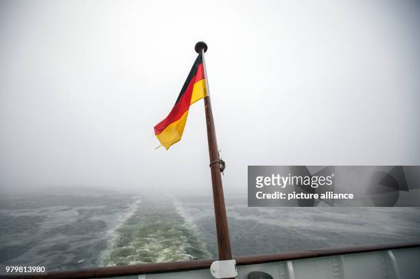 March 2018, Germany, Schaprode: The German flag waving amidst thick fog on the mast of the stern of the ferry "Vitte", while it does the crossing to...