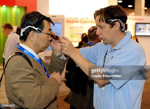 Chris Parkinson of Kopin Corp., software manager for Golden-i, helps Masao Yamasawa try out a Golden-i head-mounted computer featuring a virtual...