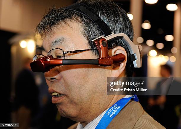 Masao Yamasawa tries out a Golden-i head-mounted computer by Kopin Corp., featuring a virtual 15-inch laptop screen that works with voice commands at...