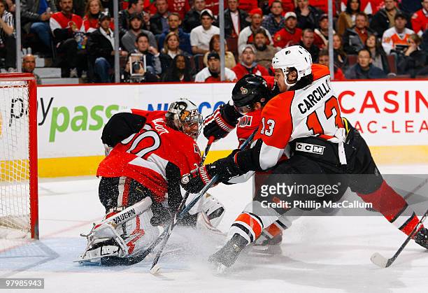 Brian Elliot of the Ottawa Senators makes a pad save while teammate Anton Volchenkov battles with Dan Carcillo of the Philadelphia Flyers for the...
