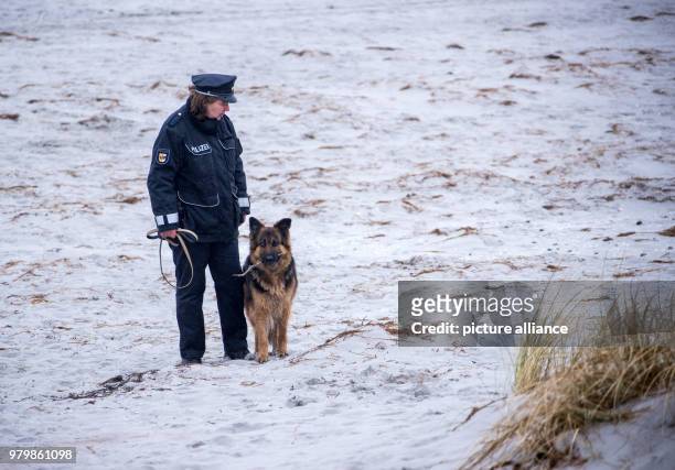 March 2018, Germany, Hiddensee: Island police officer Martina Dominik and her German Shepherd dog Maggie on duty despite the rain at the beach on the...