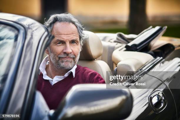 portrait of grey-haired man sitting in convertible car - welvaart stockfoto's en -beelden