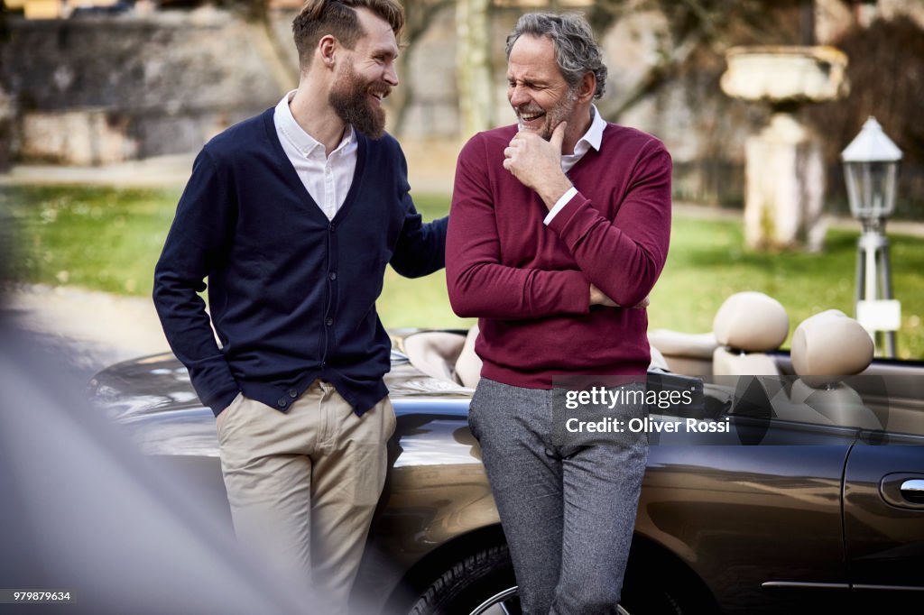 Happy father and adult son at convertible car