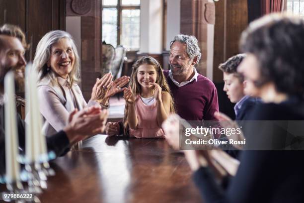 happy family sitting around wooden table applauding - welvaart stockfoto's en -beelden