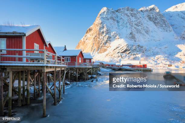 typical wood huts called rorbu surrounded by frozen the sea and snowcapped mountains, reine, lofoten islands, norway - rorbu stock pictures, royalty-free photos & images