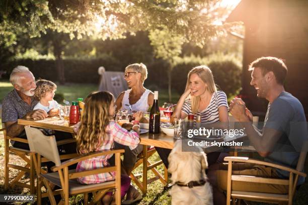 alegre extendido familia disfrutando en la conversación durante la hora del almuerzo en el patio trasero. - fiesta de jardín fotografías e imágenes de stock