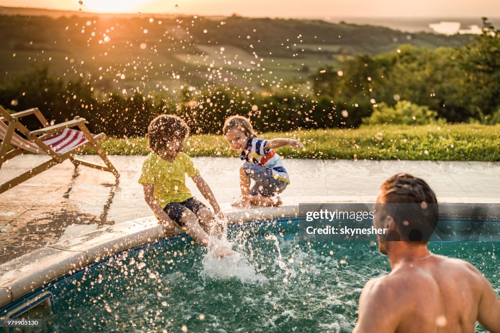 Muchachos felizes divertirse mientras está salpicada por su padre desde la piscina.