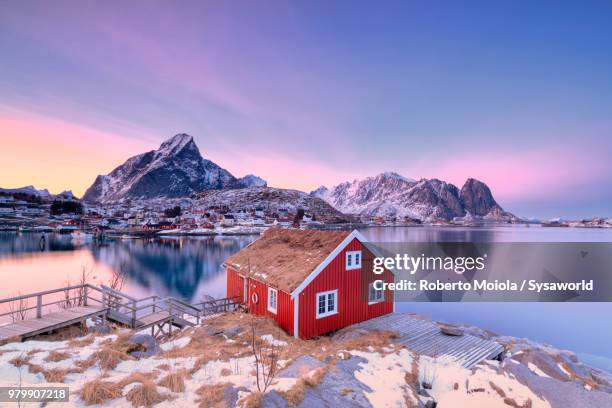 sunset on typical wood hut called rorbu surrounded by frozen the sea and snowcapped mountains, reine, lofoten islands, norway - cabin norway stock pictures, royalty-free photos & images