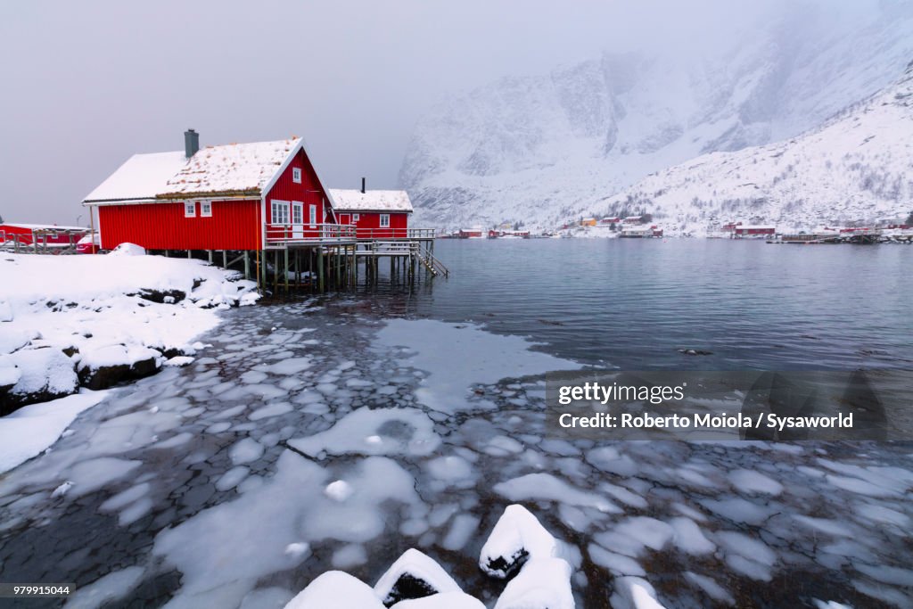 Traditional fisherman's huts called Rorbu on the icy sea surrounded by snowcapped mountains, Reine Bay, Lofoten Islands, Norway