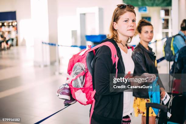 mujeres jóvenes esperando en línea en el aeropuerto - mirar alrededor fotografías e imágenes de stock