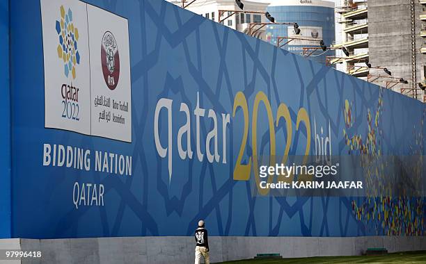 Man walks in front of a banner for Qatar's 2022 bid to host the World Cup at the Doha corniche on March 22, 2010. Qatar's bid to host a football...