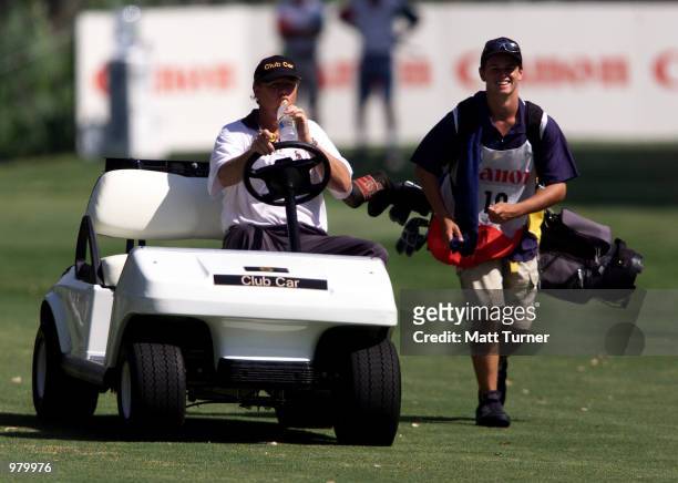 Nigel Lane of Australia, beats the heat in his motorised cart as his caddy tries to keep up during the first round of The Canon Challenge being held...