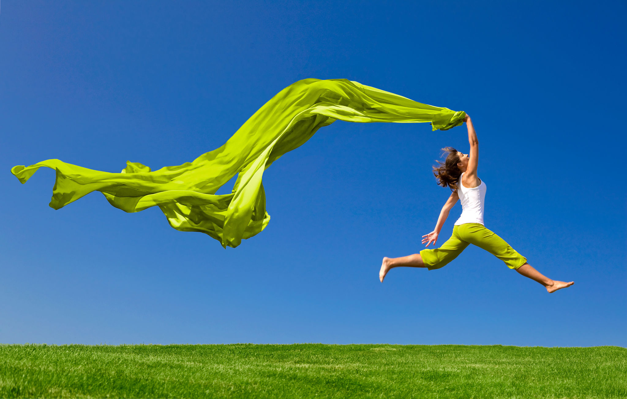 Woman jumping on green meadow with colored tissue Woman jumping on green meadow with colored tissue