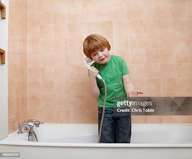 boy telephoning with showerhead in bathtub - tête penchée photos et images de collection