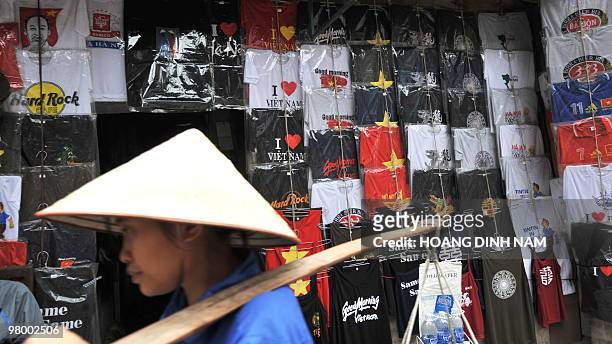 Street vendor walks past a facade of a shop covered with T-shirts in the tourist quarter of Hanoi on March 19, 2010. AFP PHOTO/HOANG DINH Nam