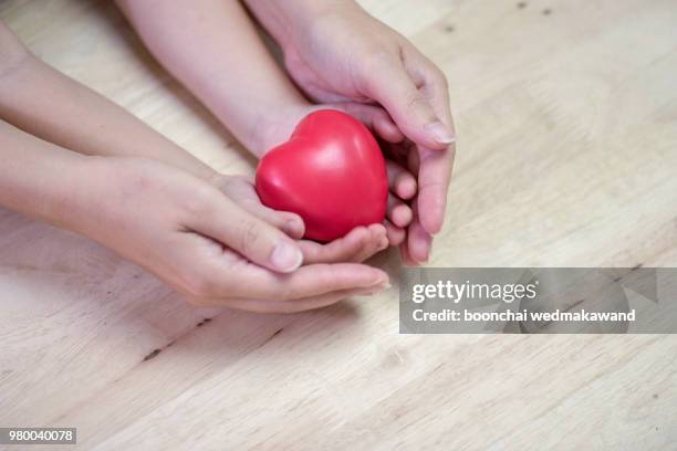 red heart in child kid and mother hands on wooden table. - world humanitarian day stock pictures, royalty-free photos & images