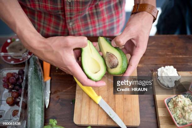 young man holding halves of avocado in kitchen - middle stock pictures, royalty-free photos & images