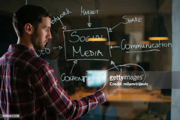 young man writing on glass wall in the office - cfo stock pictures, royalty-free photos & images