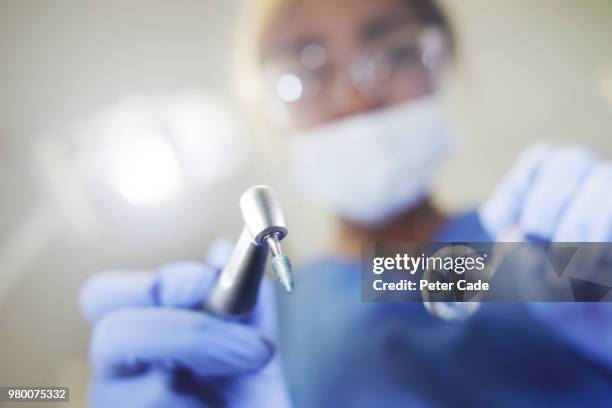 dentist looking down on camera with tools in hand - dentista foto e immagini stock