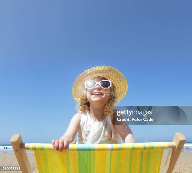 young girl looking over back of deck chair on beach - blauer hut stock-fotos und bilder