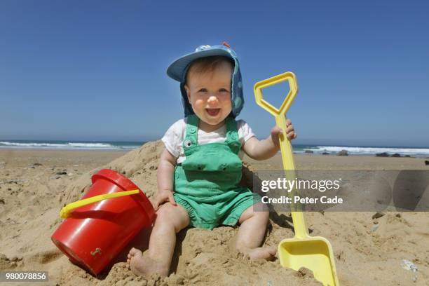 baby boy sat on beach with bucket and spade - baby boys stock pictures, royalty-free photos & images