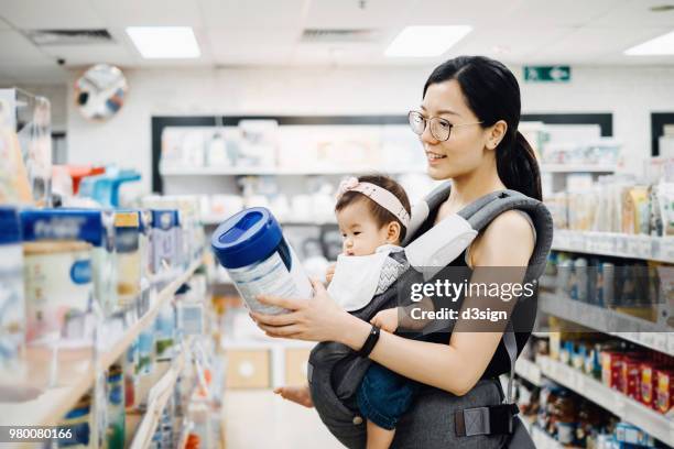 young asian mother carrying cute baby girl shopping for baby product in a shopping mall and is looking at a variety of baby formula - milchpulver stock-fotos und bilder