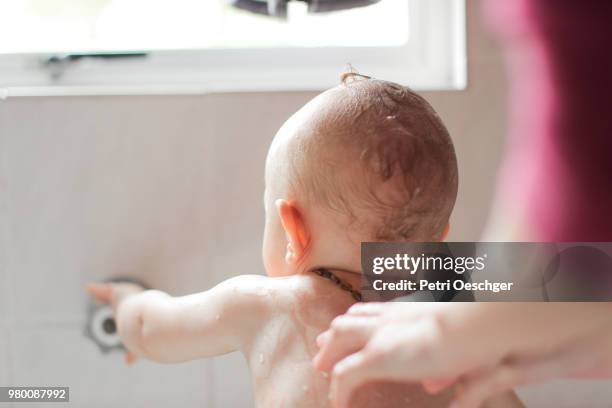 a young mother bathes her baby boy at home. - 洗礼 個照片及圖片檔