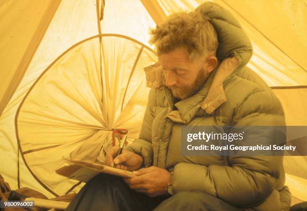 Charles Evans inside tent writing notes and wearing a down jacket, Nepal, March 1953. Mount Everest Expedition 1953.