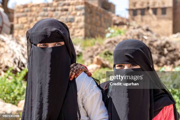 an unidentified woman and her daughters in traditional dresses walk hand in hand in the sanaa street. - yemen girl stock pictures, royalty-free photos & images