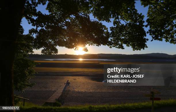 Man sits on a bridge on the lakeside of the Forggensee lake, that is partly dry due to renovation works on its dam, as sun sets over Schwangau,...