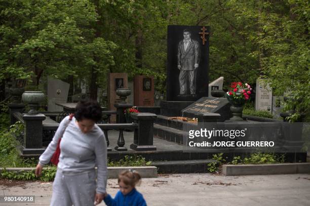 This picture taken on June 19, 2018 shows a woman with her daughter walking past the tombstone of the Russian mafia gangster Mikhail Kuchin in...