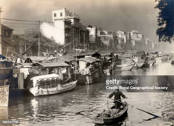 Canton after the rain, Chinese woman sculling boat past Tan houseboats and buildings of river front in Canton, taken in the 1930's, China, 1930.